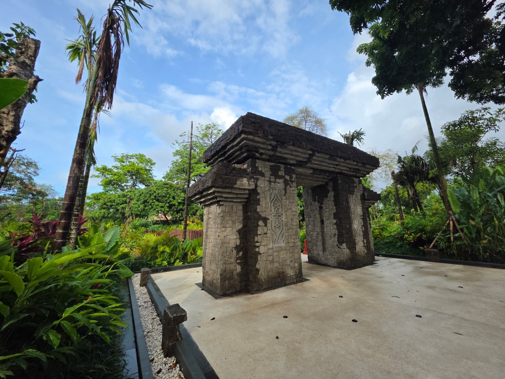A stone structure resembling a traditional Balinese gate surrounded by lush greenery in the Ethno Botanic Gardens, Sanur, Bali.